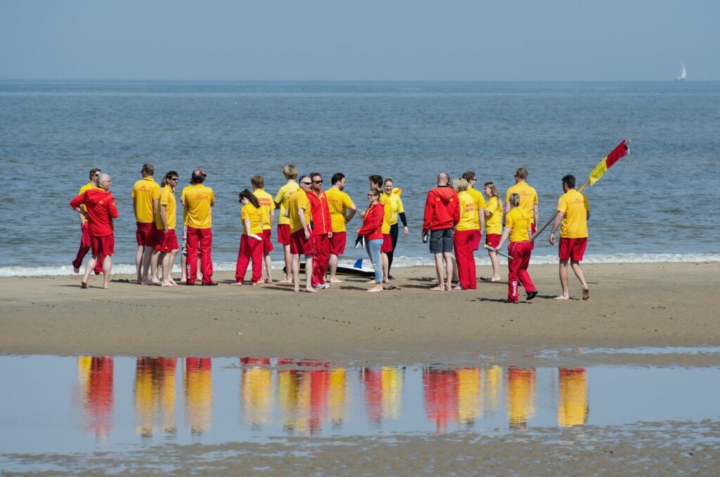 Lifeguards in yellow and red uniforms gathered on a sunny beach for safety training.
